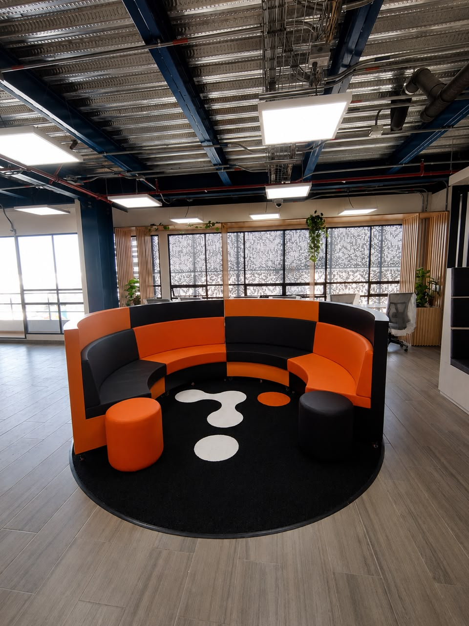 Oficina con mobiliario circular en naranja y negro y techo técnico expuesto