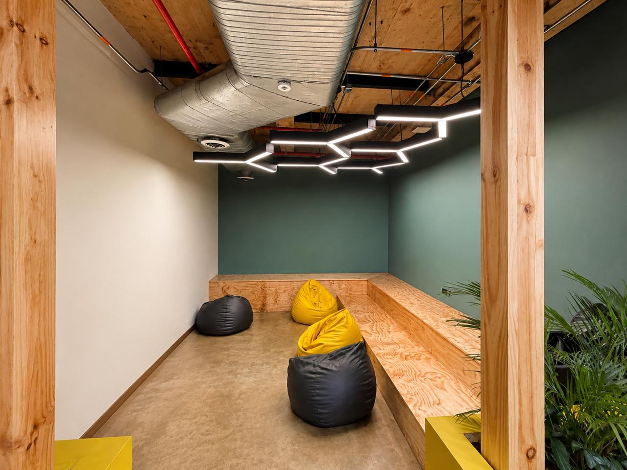 Lounge corporativo con graderías en madera, pufs y luminaria lineal en zigzag