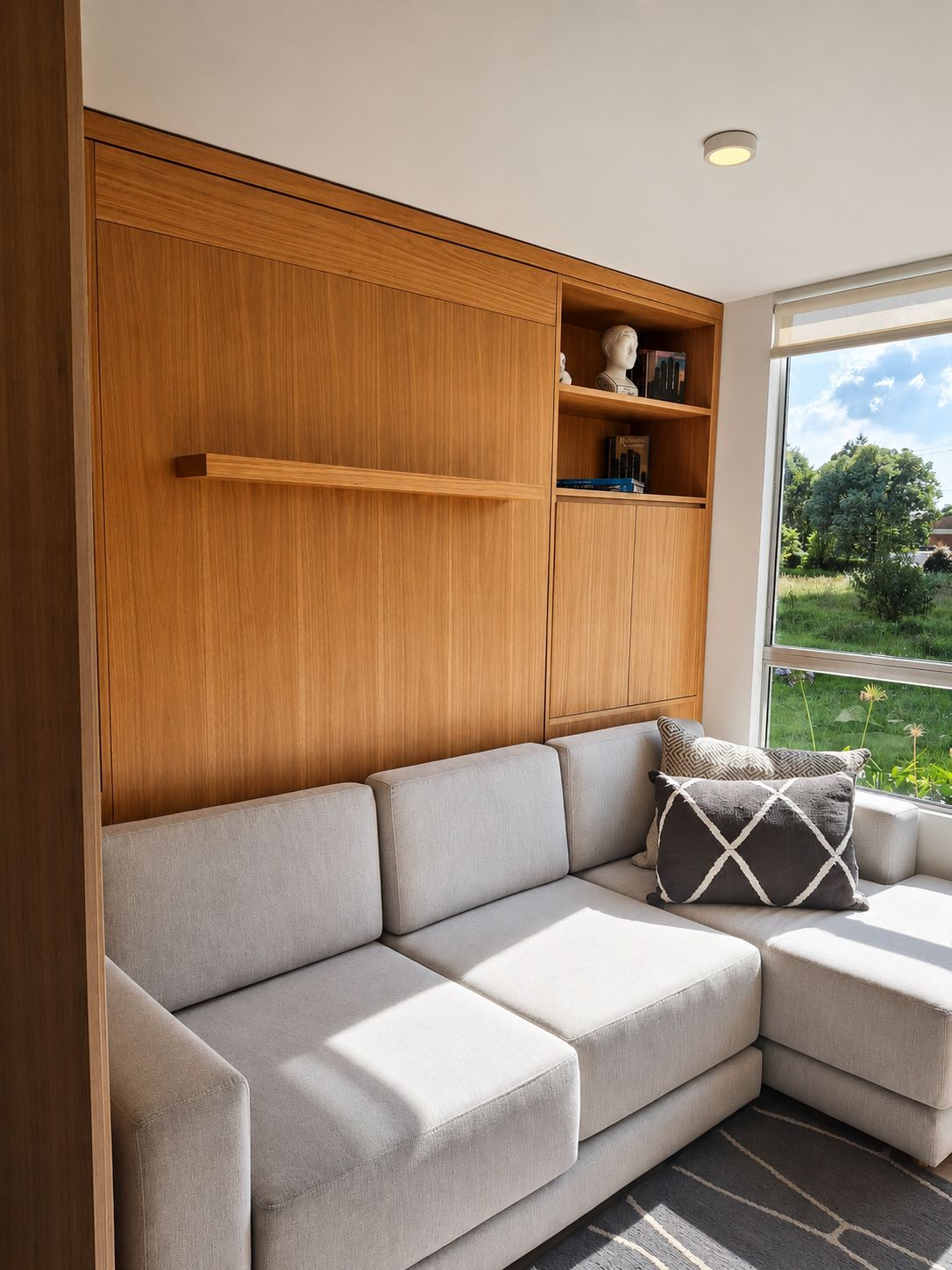 Sala con sofá gris y mueble de madera de piso a techo con nichos y almacenamiento cerrado